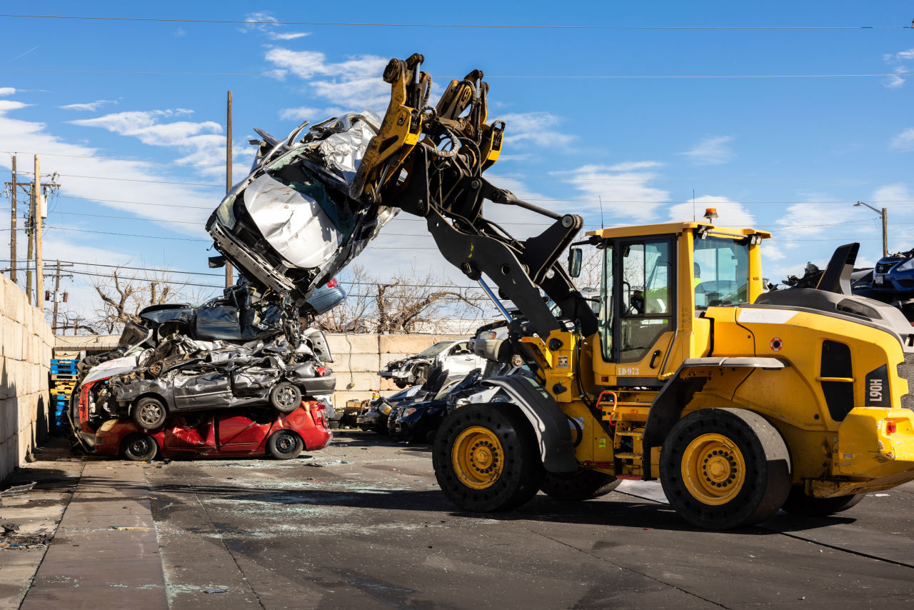 Wheel loader with a grapple lifting a crushed junk car at a Stars & Stripes Scrap Metal yard